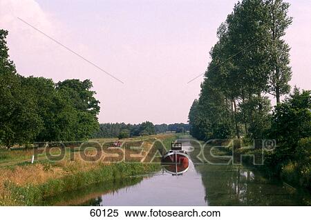 Stock Photography - Motorboat moored in canal on rural landscape, Nordgeorgsfehn, Uplengen, Lower Saxony, Germany . Fotosearch