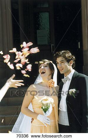 Stock Photograph - Person's hand throwing flower petals on newlywed couple . Fotosearch