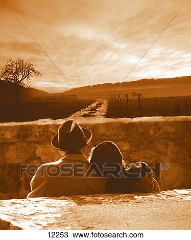 Stock Image - Rear view of senior couple sitting on bench . Fotosearch