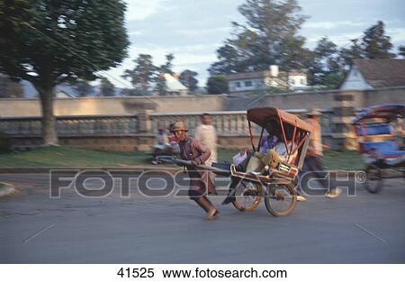 Side profile of man pulling tourists in rickshaw on road, Antsirabe, Madagascar View Large Photo Image Stock Photography - Side profile of man pulling tourists in rickshaw on road, Antsirabe, Madagascar . Fotosearch