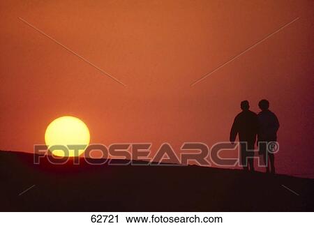 Stock Image - Silhouette of couple walking at dusk . Fotosearch