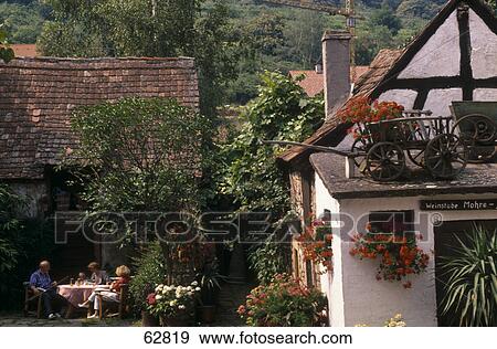 Three people sitting at table in front of house, Neustadt-Hambach, Rhineland-Palatinate, Germany View Large Photo Image Stock Photo - Three people sitting at table in front of house, Neustadt-Hambach, Rhineland-Palatinate, Germany . Fotosearch