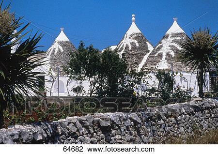 Stock Image - Trees near trulli the traditional stone dwellings with conical roofs, Alberobello, Bari, Puglia, Italy . Fotosearch