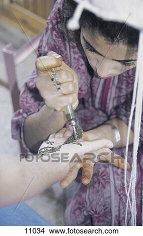 Picture - Woman painting henna tattoo on another woman's hand, Morocco . Fotosearch
