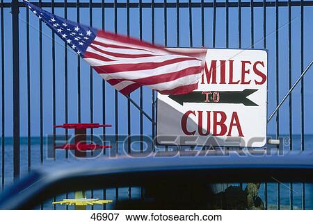 Stock Photo - American flag with signboard of Cuba Southernmost Point, Key West, Florida, USA . Fotosearch