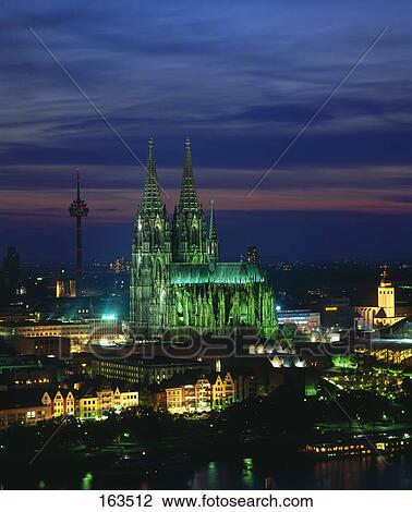 Stock Image - Buildings with cathedral lit up at night, Cologne Cathedral, Cologne, Rhine River, North Rhine-Westphalia, Germany . Fotosearch