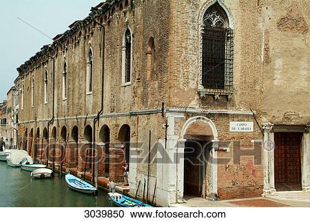 Stock Image - Canal with moored boats and Arcades of a Venetian convent building, Italien . Fotosearch