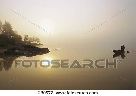 Stock Image - Man rowing boat on Bjorndalsvatnet Lake at sunrise, Bremanger, Norway . Fotosearch
