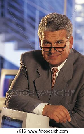 Stock Photograph - Portrait of a businessman leaning on computer in an office . Fotosearch
