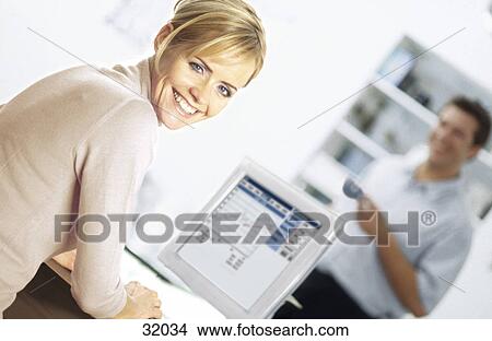 Picture - Portrait of a young woman working on a computer with a young man standing in the background . Fotosearch