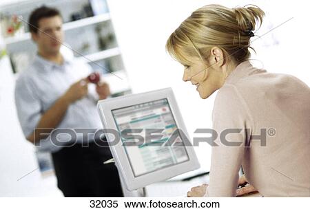 Stock Photography - Side profile of a young woman working on a computer with a young man standing in the background . Fotosearch