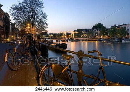 Bicycles parked at riverbank with bridge in background, Magere Brug, Amstel River, North Holland, Amsterdam, Netherlands View Large Photo Image Stock Photograph - Bicycles parked at riverbank with bridge in background, Magere Brug, Amstel River, North Holland, Amsterdam, Netherlands . Fotosearch