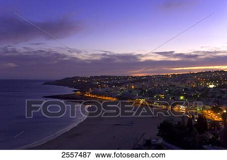 Stock Photo - Buildings lit up at waterfront, Praia da Luz, Algarve, Portugal . Fotosearch