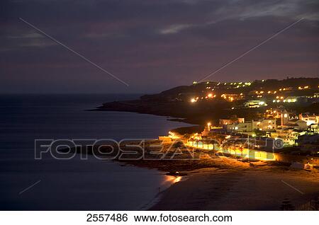 Stock Photograph - Buildings lit up at waterfront, Praia da Luz, Algarve, Portugal . Fotosearch
