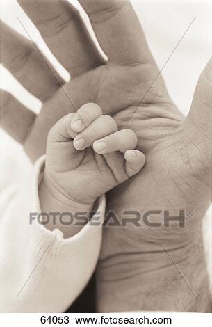 Stock Image - Close-up of a man's hand touching his baby's hand . Fotosearch