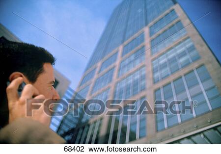 Stock Image - Close-up of businessman talking on mobile phone in front of office building . Fotosearch