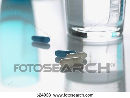 Stock Image - Close-up of capsules and glass of water . Fotosearch