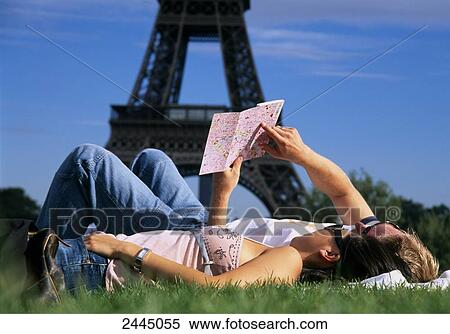Stock Photography - Couple lying in lawn and looking at map, Paris, Ile-de-France, France . Fotosearch