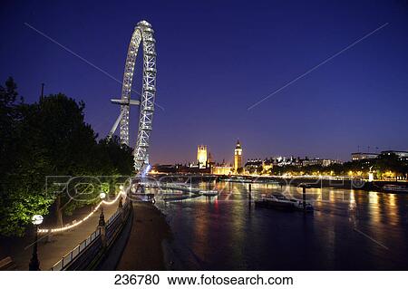 Stock Image - Ferris wheel and buildings lit up at night, Millennium Wheel, Thames River, London, England . Fotosearch
