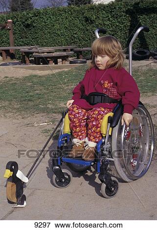 Stock Photo - Girl sitting in wheelchair and playing with toy, Germany . Fotosearch