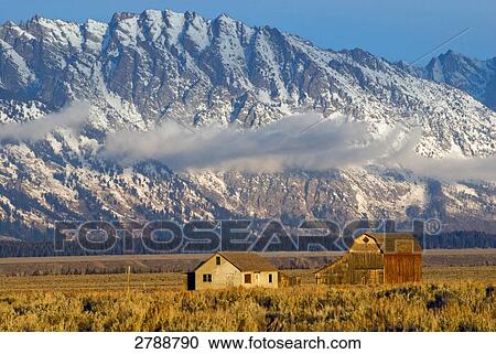 Stock Image - Houses in field with mountain in background, Grand Teton National Park, Wyoming, USA . Fotosearch