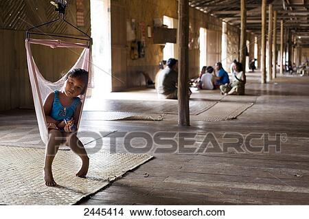 Picture - Iban girl sitting on swing in hallway, Iban, Borneo, Indonesia . Fotosearch