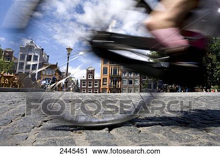 Stock Image - Low section view of person cycling with buildings in city, North Holland, Amsterdam, Netherlands . Fotosearch