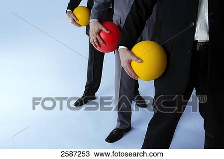 Stock Image - Low section view of three businesspeople holding balls . Fotosearch