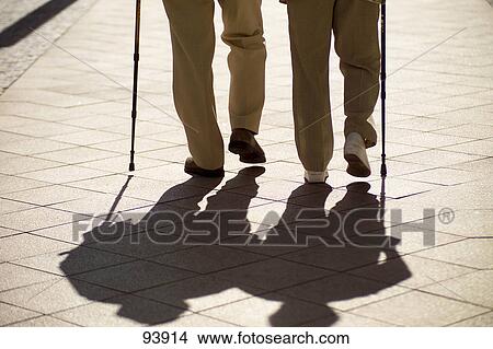 Picture - Low section view of two men walking with canes on pavement . Fotosearch
