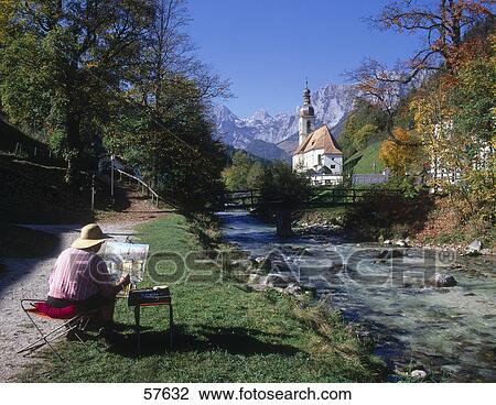 Stock Image - Man painting picture of church at riverside, St. Sebastian Church, Ramsau bei Berchtesgaden, Berchtesgadener Land, Bavaria, Germany . Fotosearch