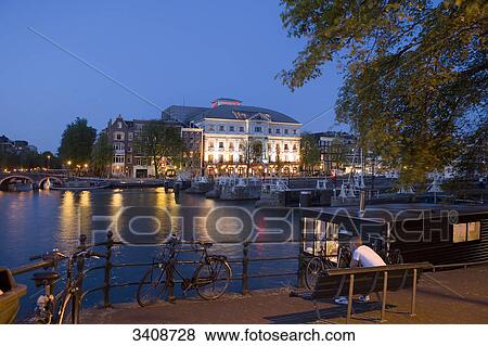Man sitting on a bench at the riverside, Carre Theatre in the background, Amsterdam, Netherlands View Large Photo Image Stock Photo - Man sitting on a bench at the riverside, Carre Theatre in the background, Amsterdam, Netherlands . Fotosearch