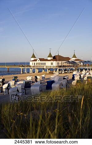 Stock Image - Marram grass and hooded beach chairs on beach with pier in background, Ahlbeck, Usedom, Mecklenburg-West Pomerania, Germany . Fotosearch