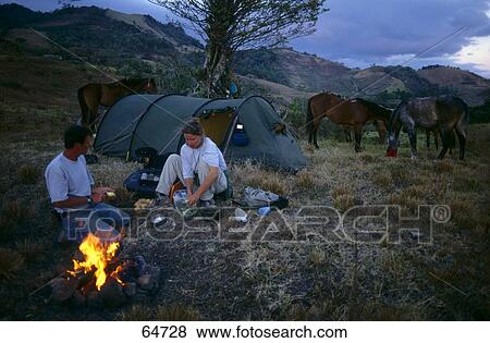 Stock Photo - Mid adult couple cooking food while camping on landscape . Fotosearch
