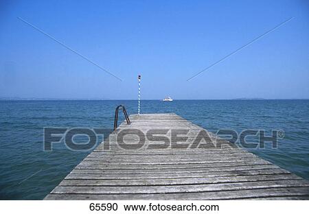 Stock Image - Pier leading to lake, Lake Garda, Italy . Fotosearch