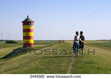 Rear view of two people standing near lighthouse in field, Pilsum, Lower Saxony, Germany View Large Photo Image Stock Image - Rear view of two people standing near lighthouse in field, Pilsum, Lower Saxony, Germany . Fotosearch