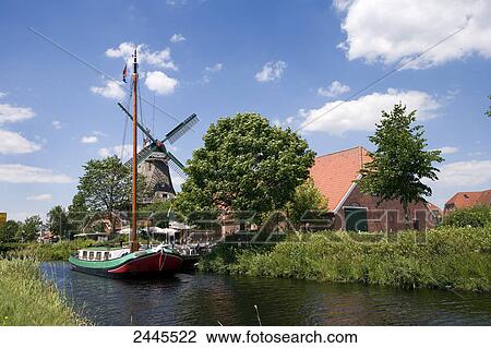 Stock Image - Sailboat in canal with industrial windmill in background, Ostgrossefehn, Lower Saxony, Germany . Fotosearch
