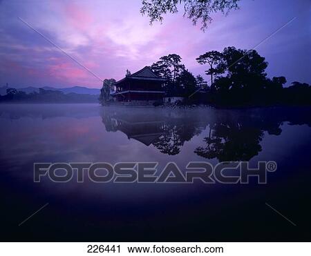 Stock Image - Silhouette of villa and trees reflected in lake at dusk, Bishu Shanzhuang, Chengde, China . Fotosearch