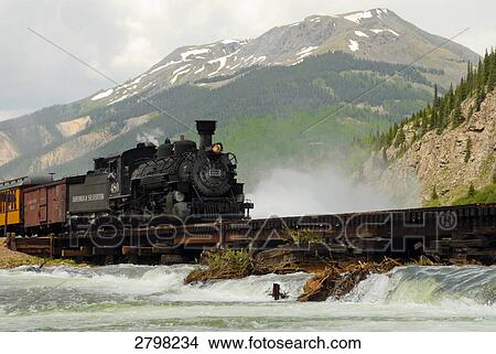 Picture - Train moving on track passing through river, Silverton, Durango, La Plata County, Colorado, USA . Fotosearch