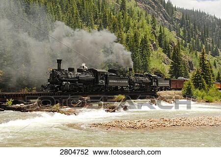 Stock Image - Train moving on track passing through river, Colorado, USA . Fotosearch