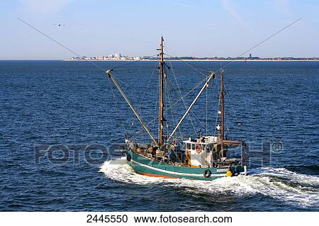 Stock Image - Trawler in sea with town in background, Norderney, Lower Saxony, Germany . Fotosearch