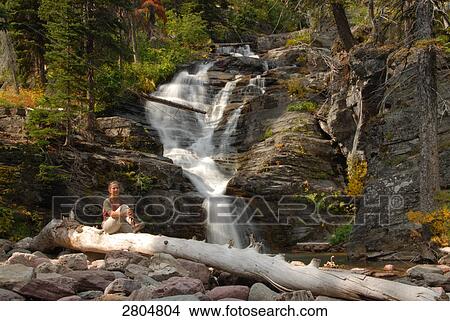 Woman sitting on log near waterfall, Glacier National Park, Montana, USA View Large Photo Image Picture - Woman sitting on log near waterfall, Glacier National Park, Montana, USA . Fotosearch