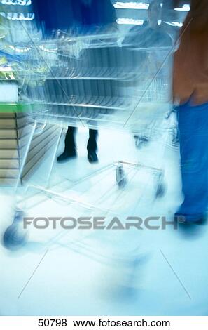 Blurred view of two people standing with shopping carts in supermarket View Large Photo Image Stock Photo - Blurred view of two people standing with shopping carts in supermarket . Fotosearch