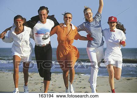 Picture - Four young women and young man running on beach . Fotosearch
