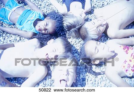Stock Image - High angle view of boys and girls lying on beach . Fotosearch