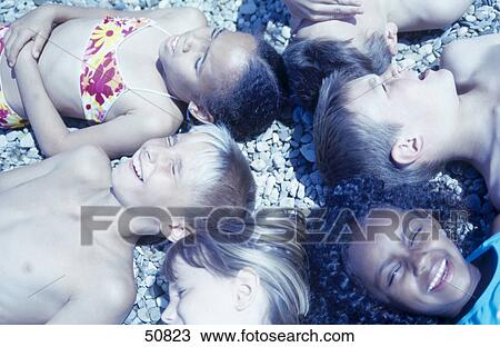 Stock Image - High angle view of boys and girls lying on beach . Fotosearch
