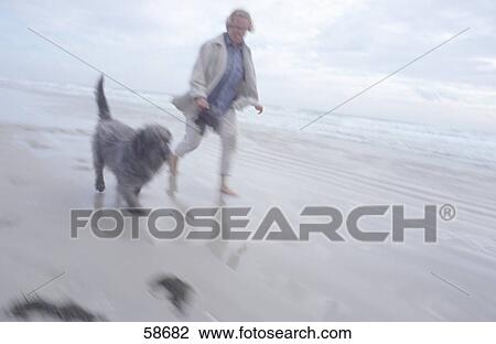 Stock Image - Man walking with dog on beach . Fotosearch