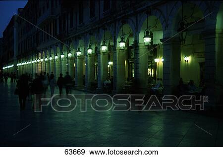 Stock Photo - Silhouette of tourists walking in front of lit up building, Corfu, Ionian Islands, Greece . Fotosearch