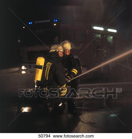 Two firemen spraying water on fire with hose View Large Photo Image Picture - Two firemen spraying water on fire with hose . Fotosearch