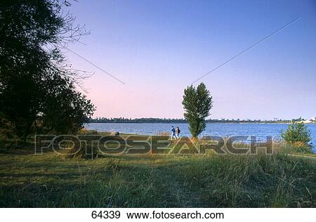 Stock Photo - Two people walking on the lakeside, Lake Kulkwitzer, Leipzig, Saxony, Germany . Fotosearch