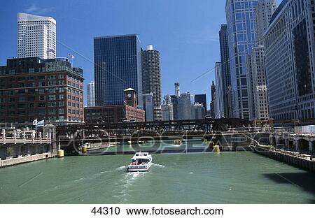 Stock Image - Boat in river near bridge in city, Wacker Drive, Chicago River, Chicago, Illinois, USA . Fotosearch